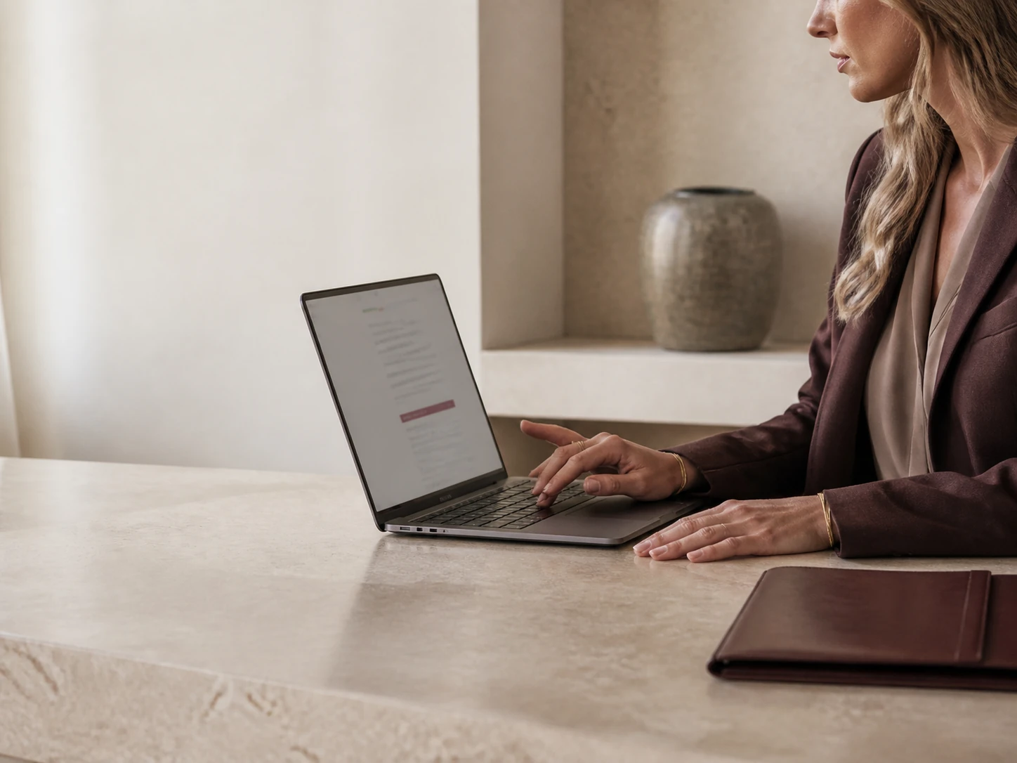 Structured taupe handbag displayed on a limestone plinth in soft natural light.